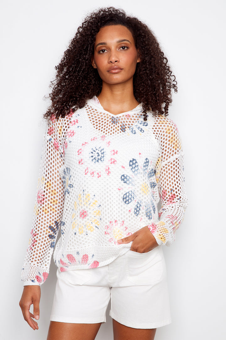 Woman wearing a floral mesh top and white shorts against a plain background