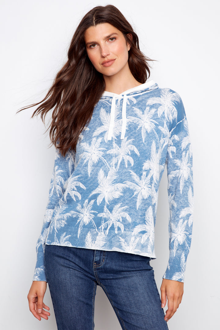 Woman wearing a blue hoodie with palm tree pattern against a white background