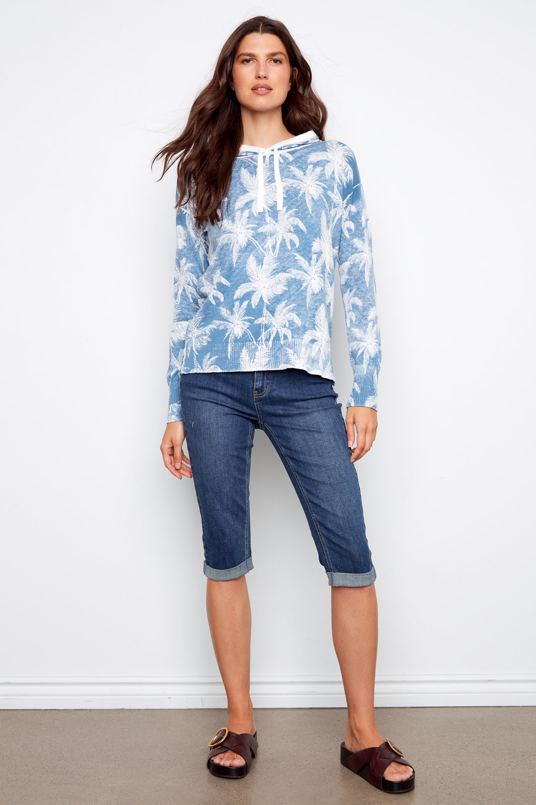 Woman wearing a blue floral blouse and blue jeans against a white background