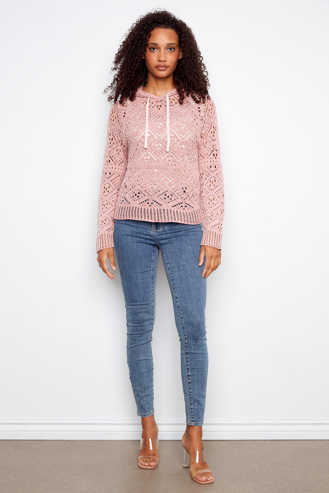 Woman wearing a pink patterned sweater and blue jeans against a white background