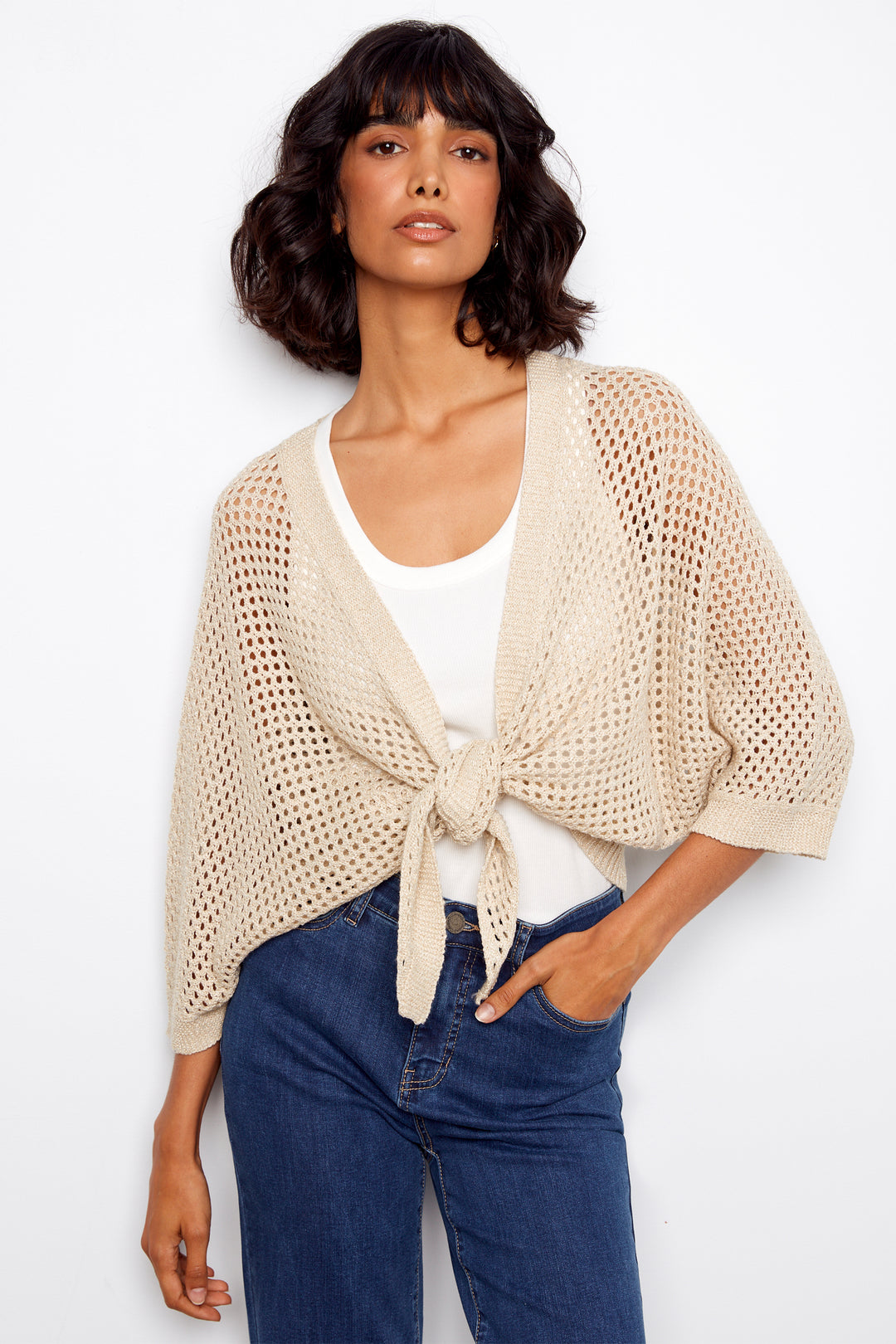 Woman wearing a beige knit cardigan front tie twist over a white top and blue jeans on a white background