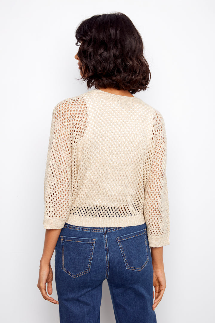 Person wearing a beige knit sweater with a textured pattern and blue jeans on a white background
