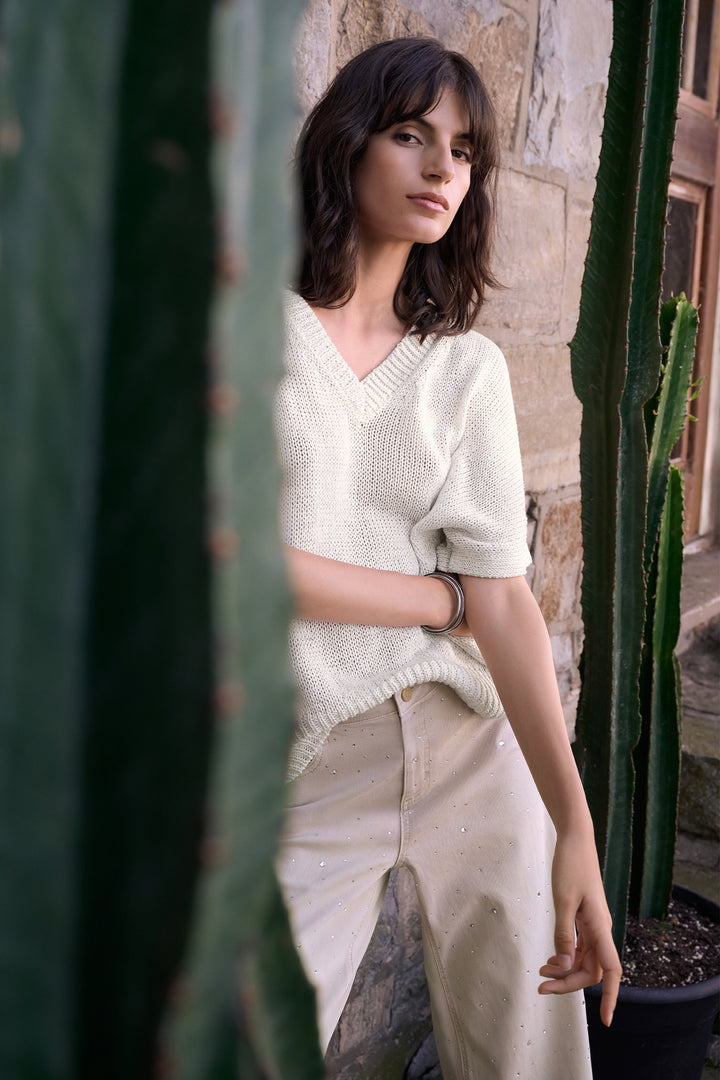 Woman in a light sweater and beige pants standing among cacti.