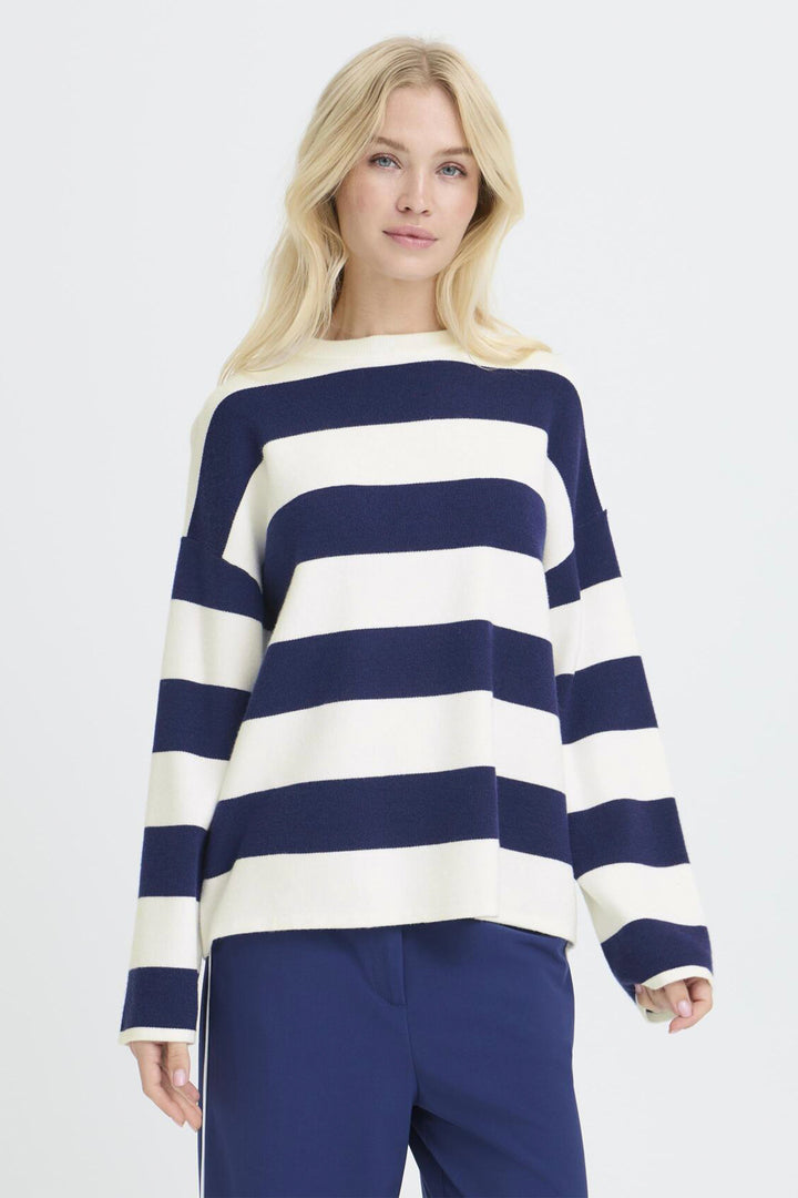 Woman wearing a navy and white striped sweater with blue pants on a light gray background