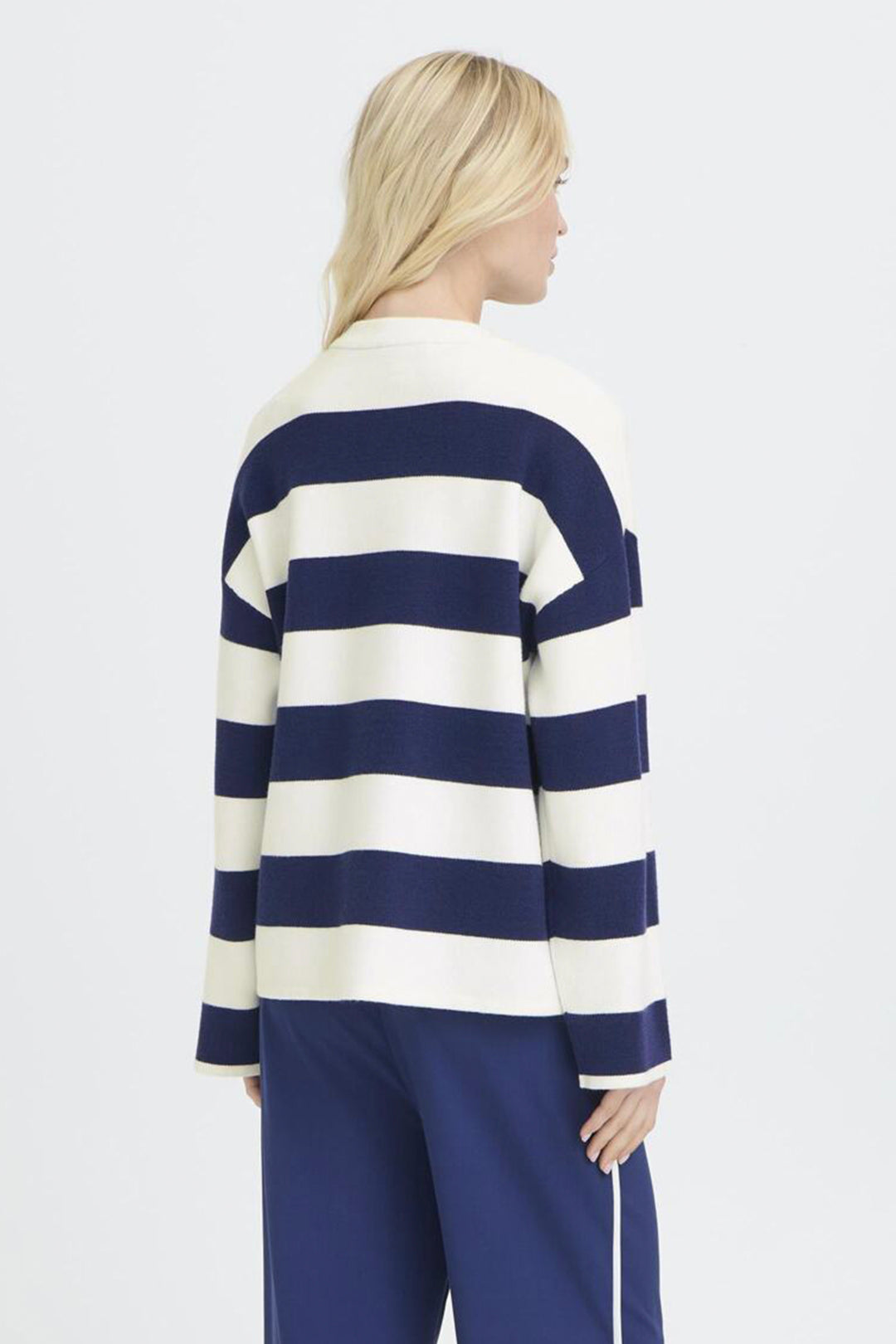 Woman wearing a navy and white striped sweater with blue pants on a light gray background