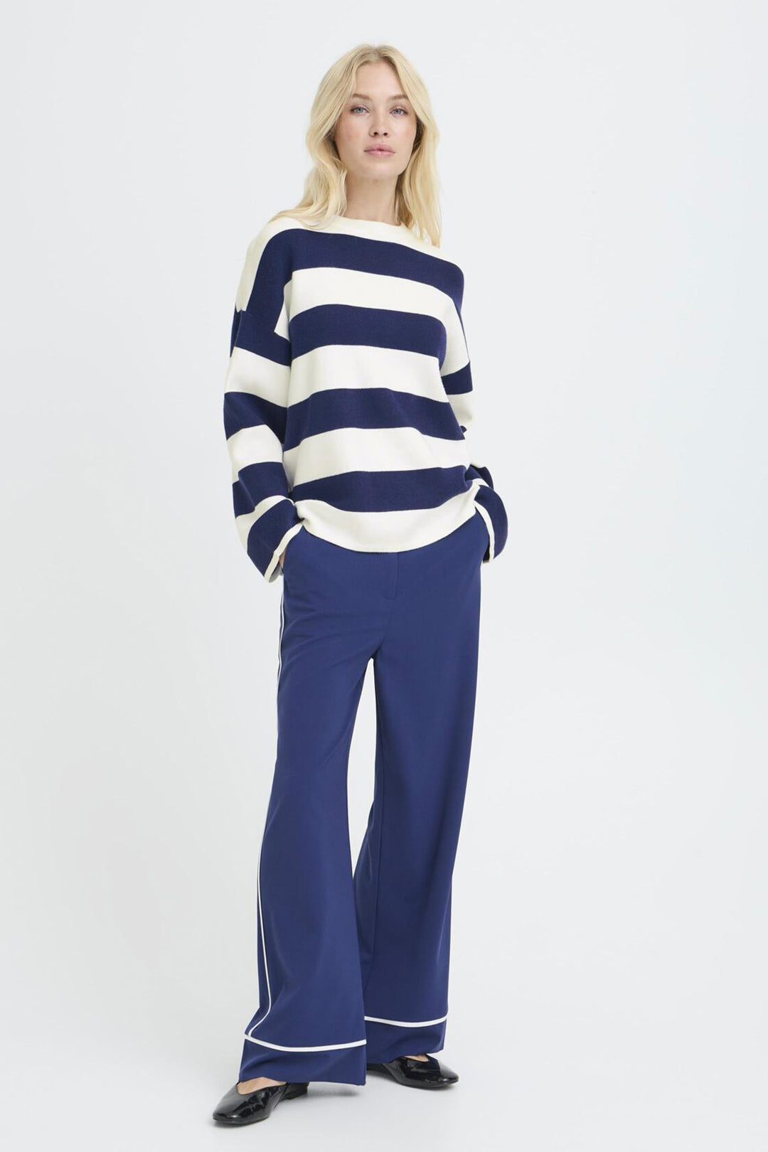 Woman wearing a navy and white striped sweater with blue pants on a white background
