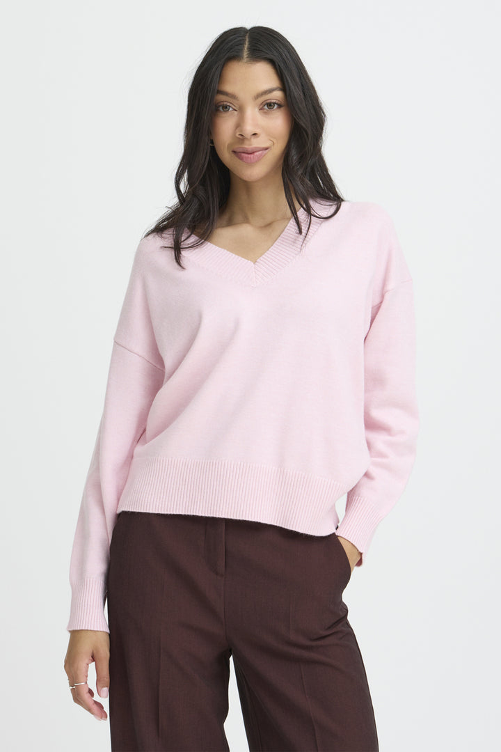 Woman wearing a light pink sweater and brown pants on a white background