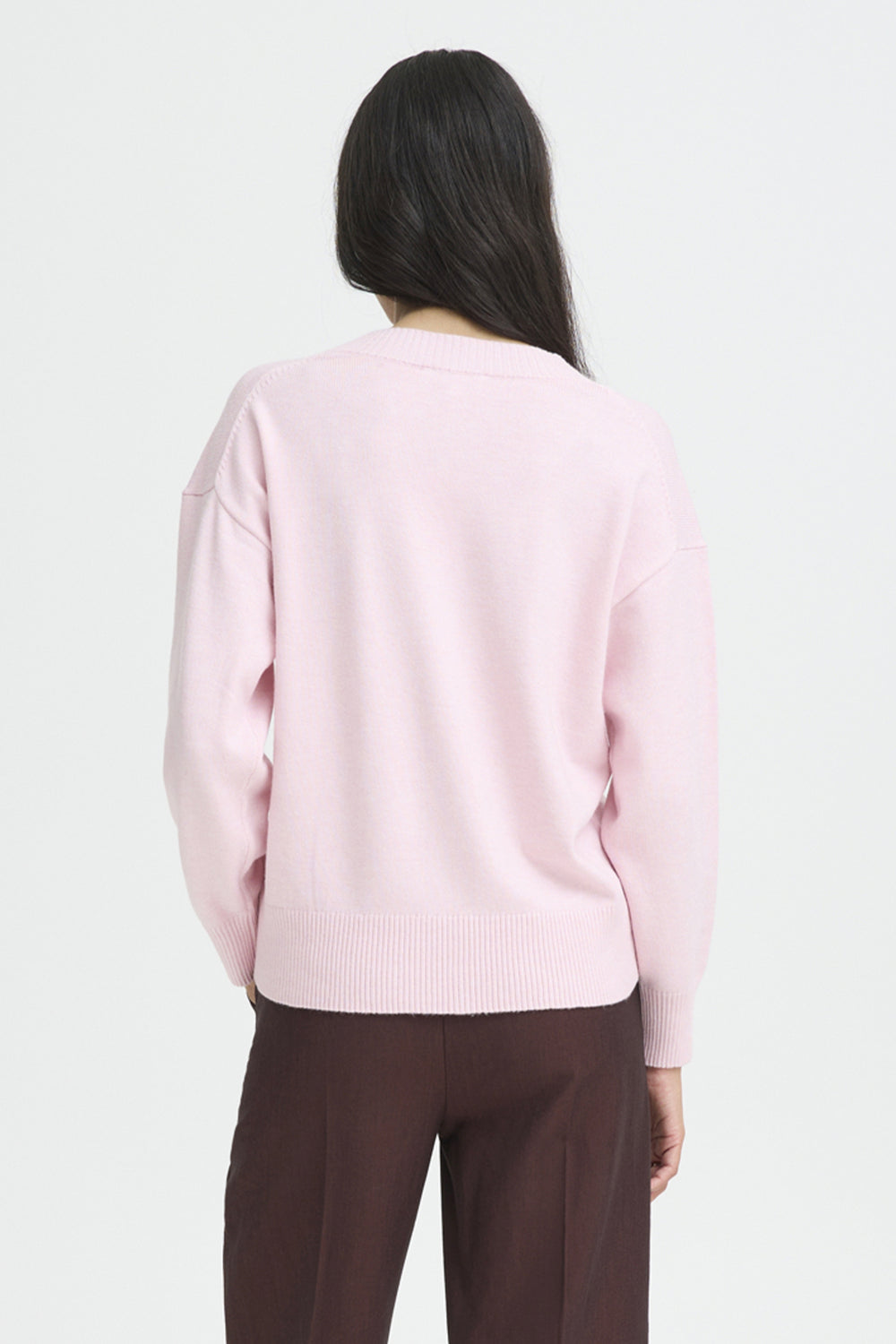 Person wearing a light pink sweater and brown pants on a white background