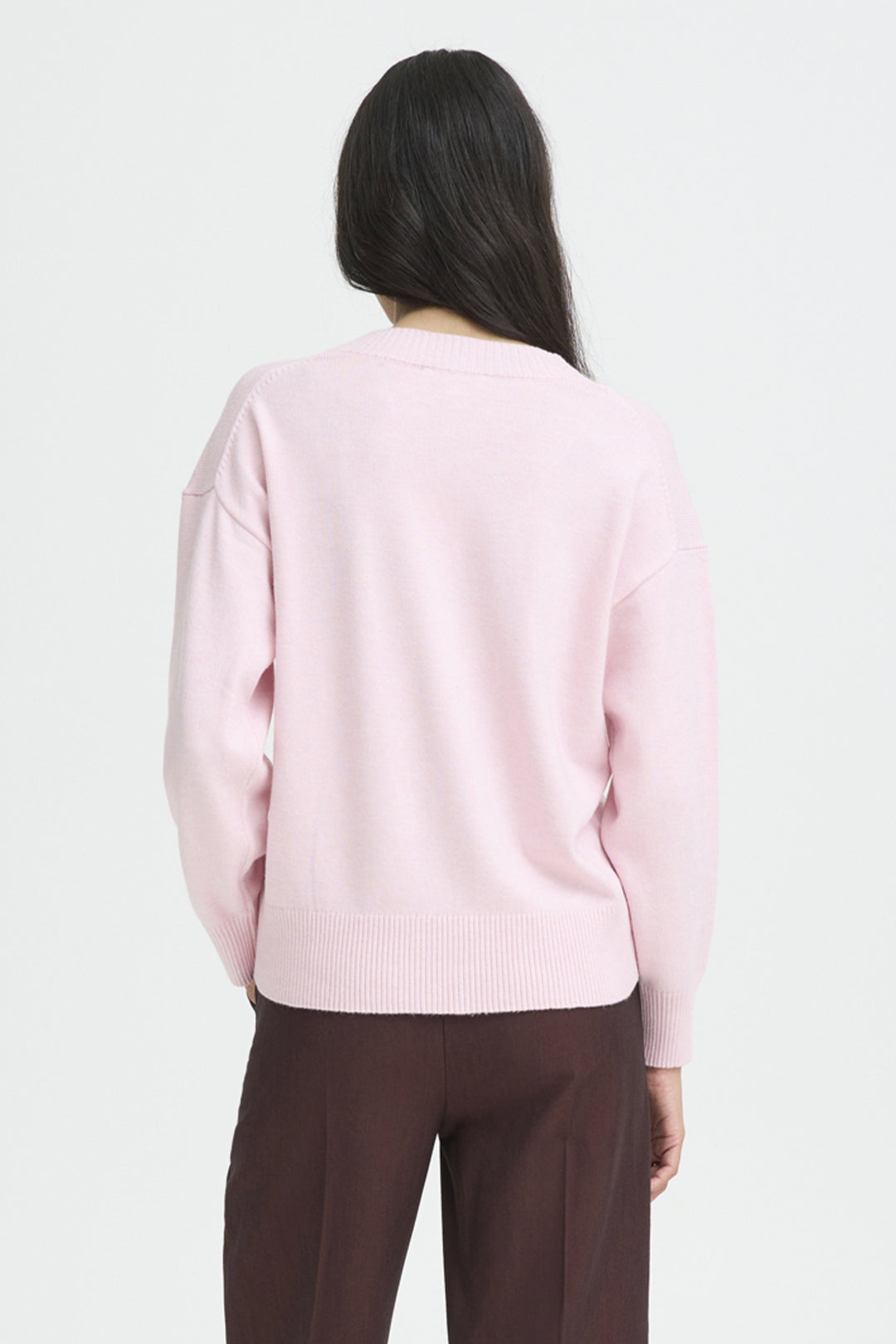 Person wearing a light pink sweater and brown pants on a white background
