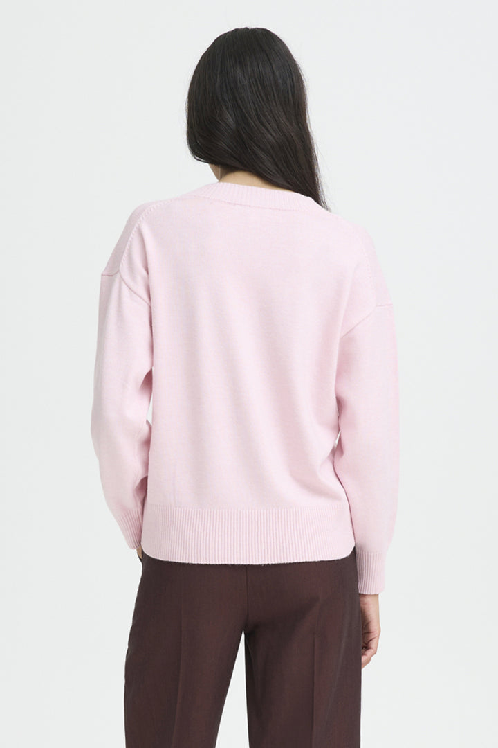 Person wearing a light pink sweater and brown pants on a white background