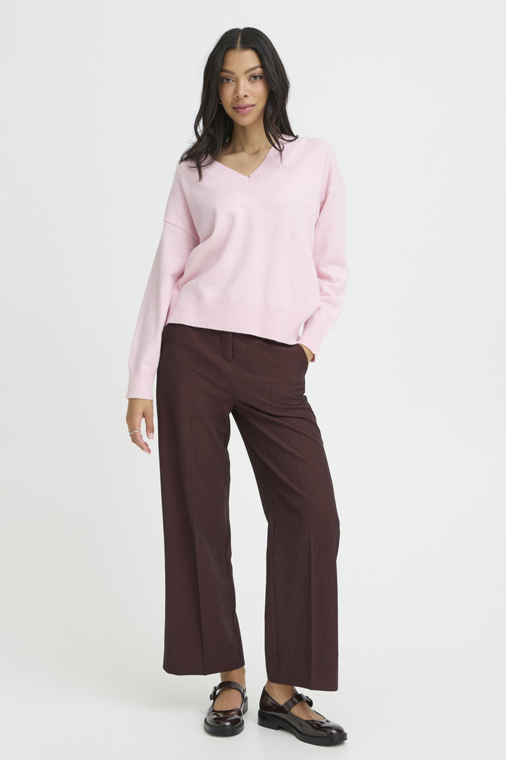 Woman wearing a light pink sweater and brown pants on a white background