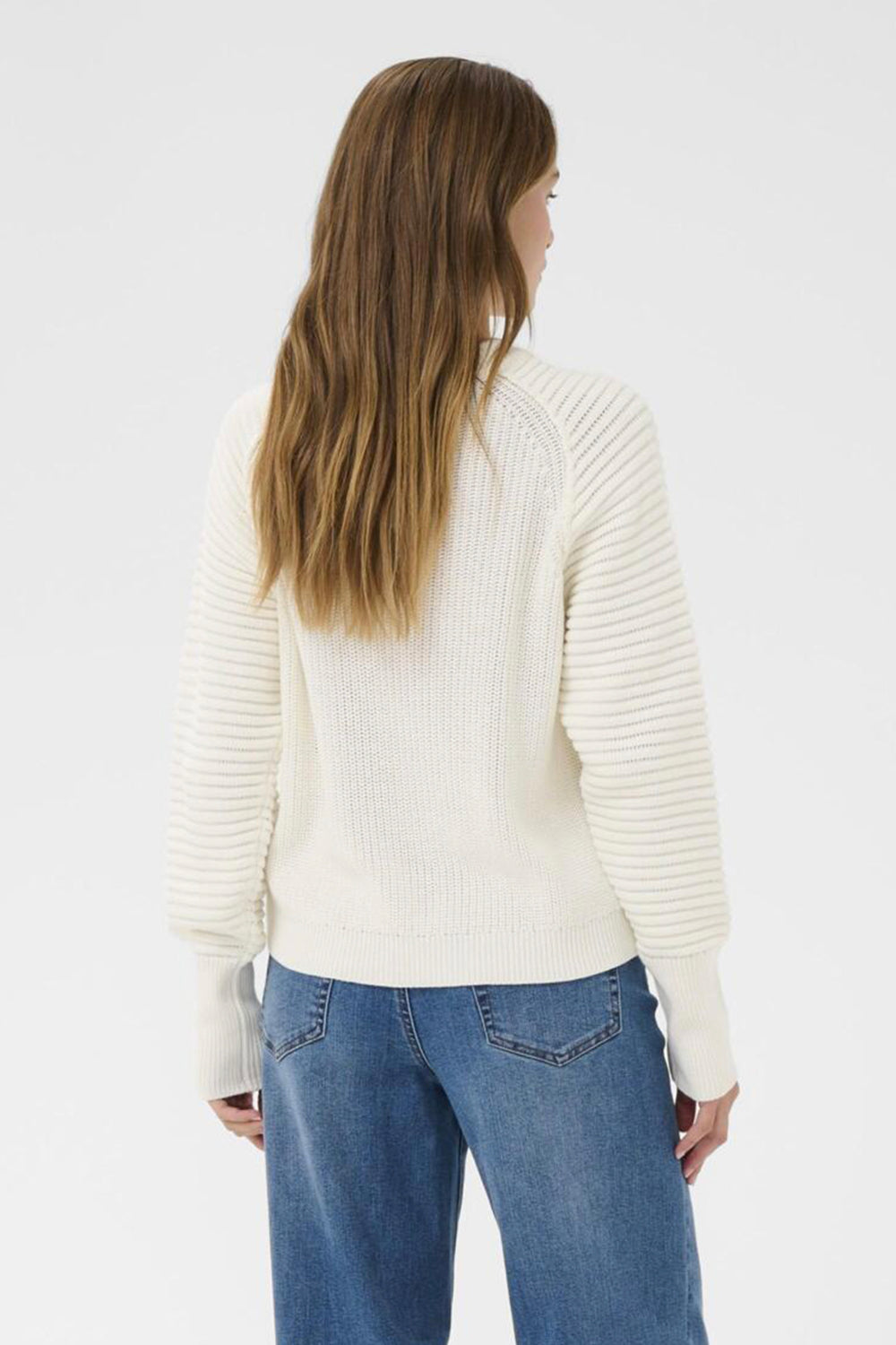 Person wearing a white ribbed sweater and blue jeans on a plain background