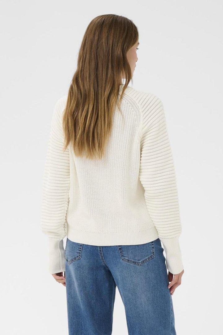 Person wearing a white ribbed sweater and blue jeans on a plain background