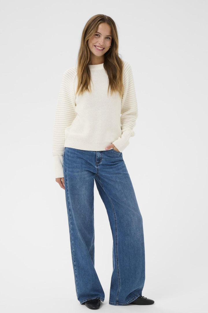 Woman wearing a white sweater and blue jeans on a white background