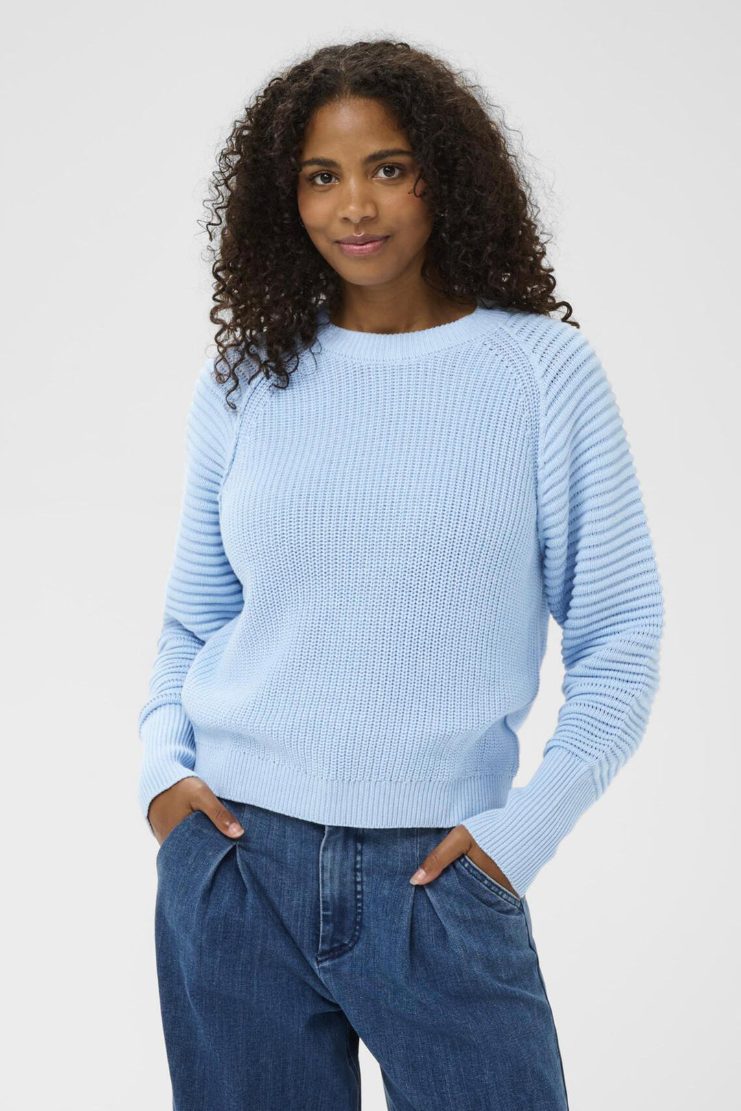 Woman wearing a light blue sweater and jeans against a plain background