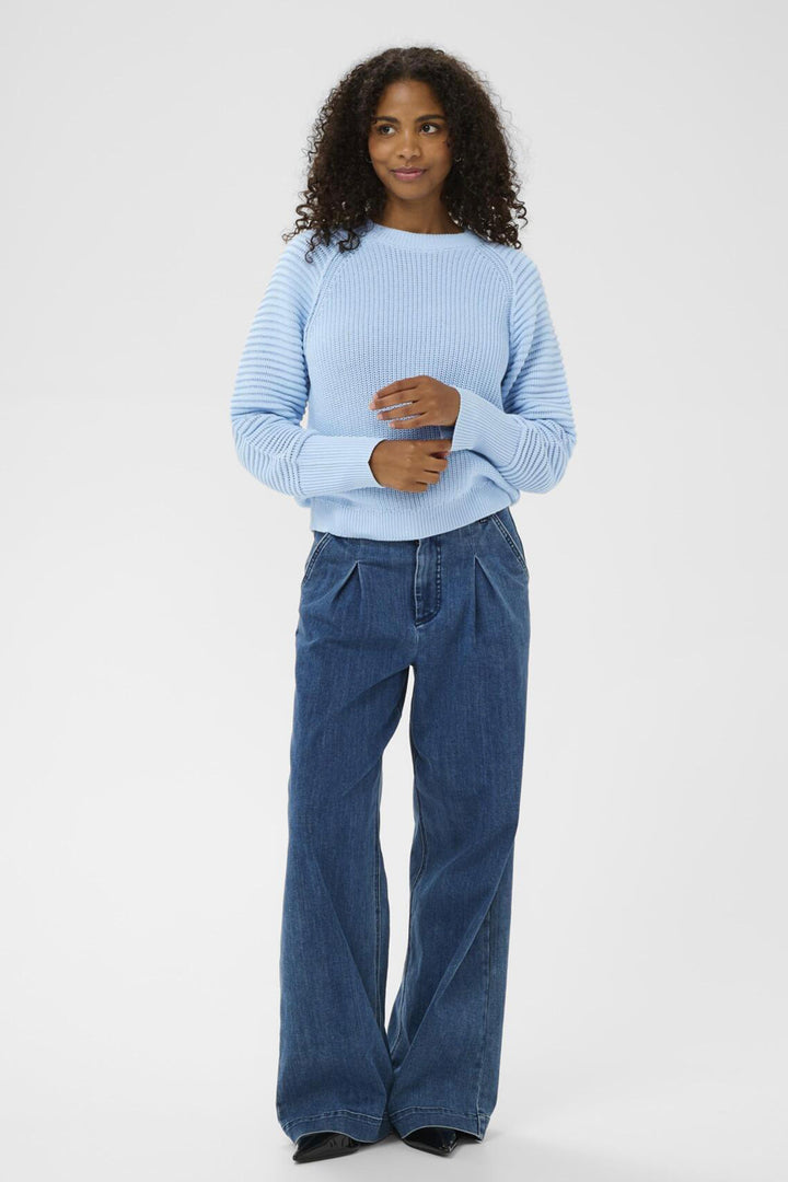 Woman wearing a light blue sweater and blue jeans on a white background