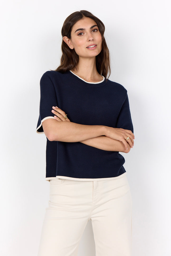 Woman wearing a navy blue top and white pants against a white background