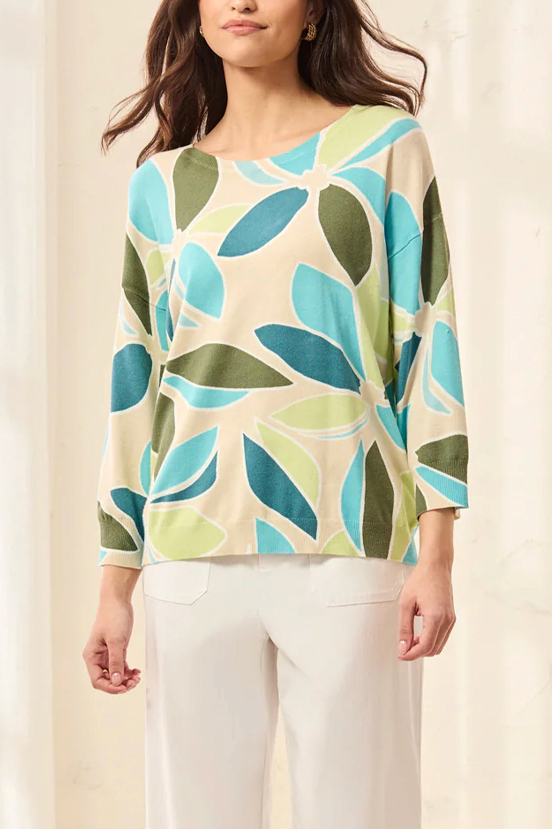 Woman wearing a colorful leaf-patterned sweater against a plain background