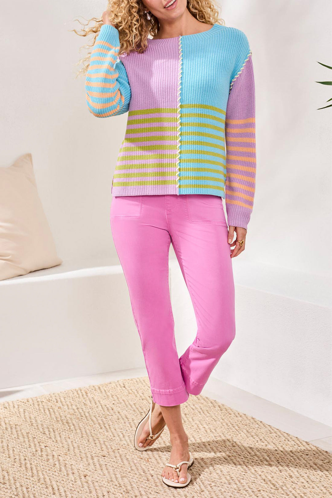 Woman wearing a colorful sweater and pink pants in a minimal indoor setting