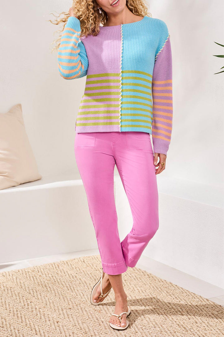 Woman wearing a colorful sweater and pink pants in a minimal indoor setting