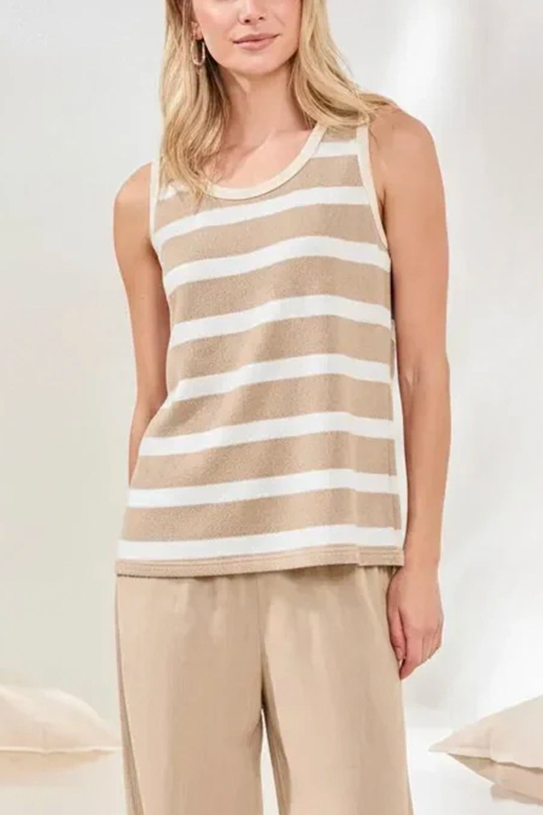 Woman wearing a beige and white striped tank top with beige pants on a light background