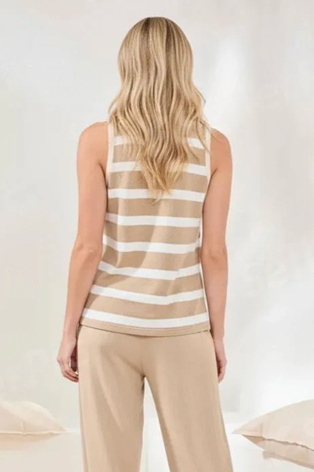 Woman wearing a beige and white striped tank top and beige pants on a light background