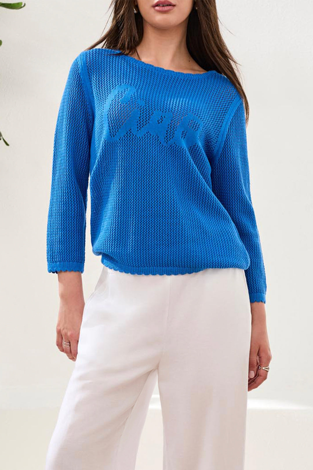 Person wearing a blue sweater with text and white pants on a light background