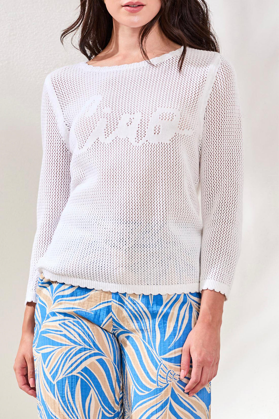 Woman wearing a white knit sweater with a patterned blue and yellow pants against a plain background