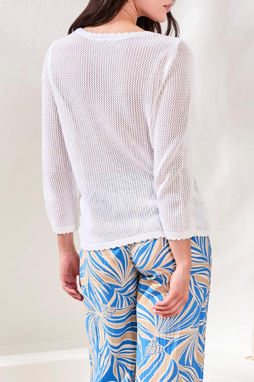 Woman wearing a white textured sweater and blue patterned pants against a plain background