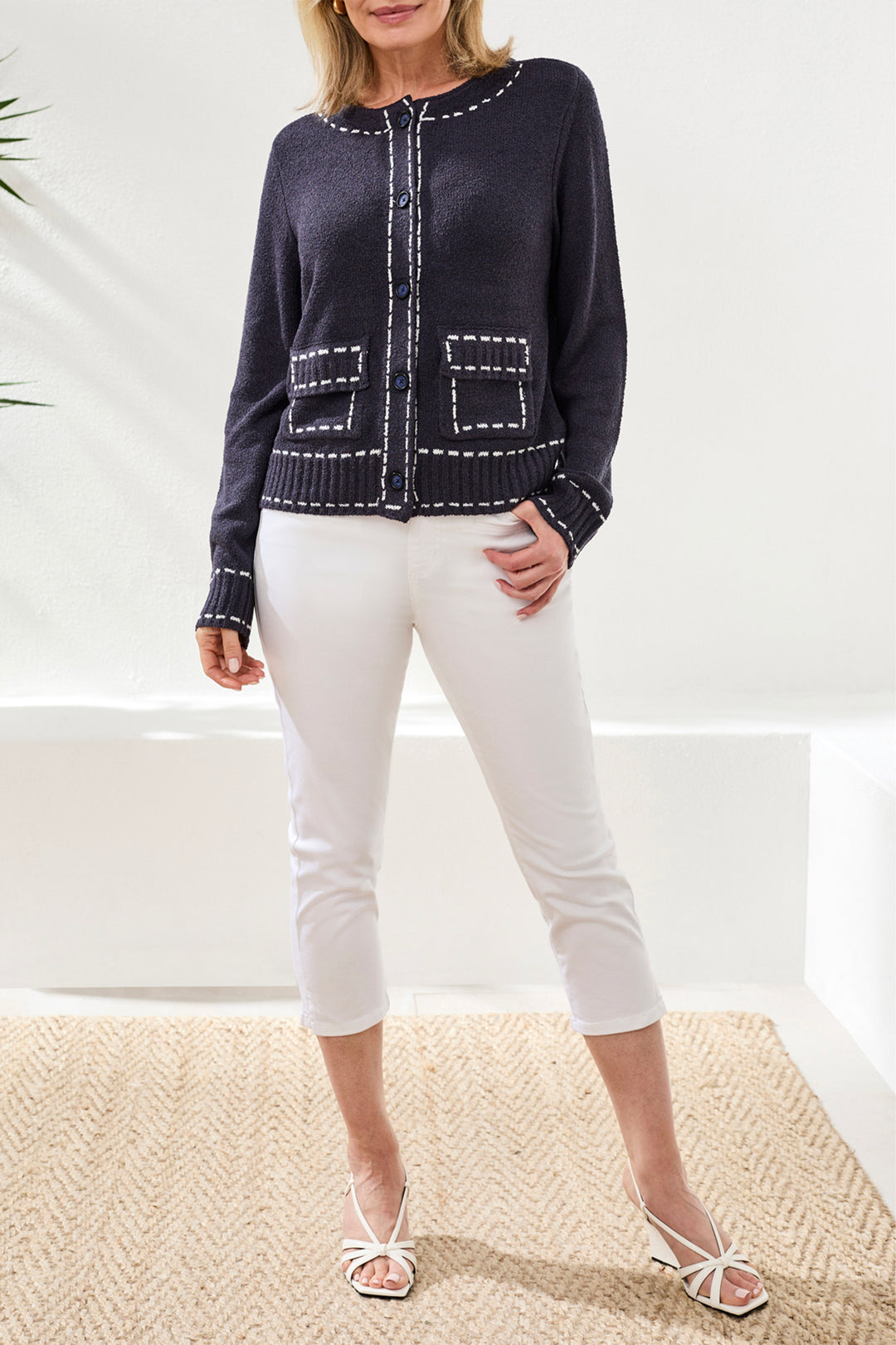 Woman wearing a navy blue sweater with white trim and white pants on a neutral background