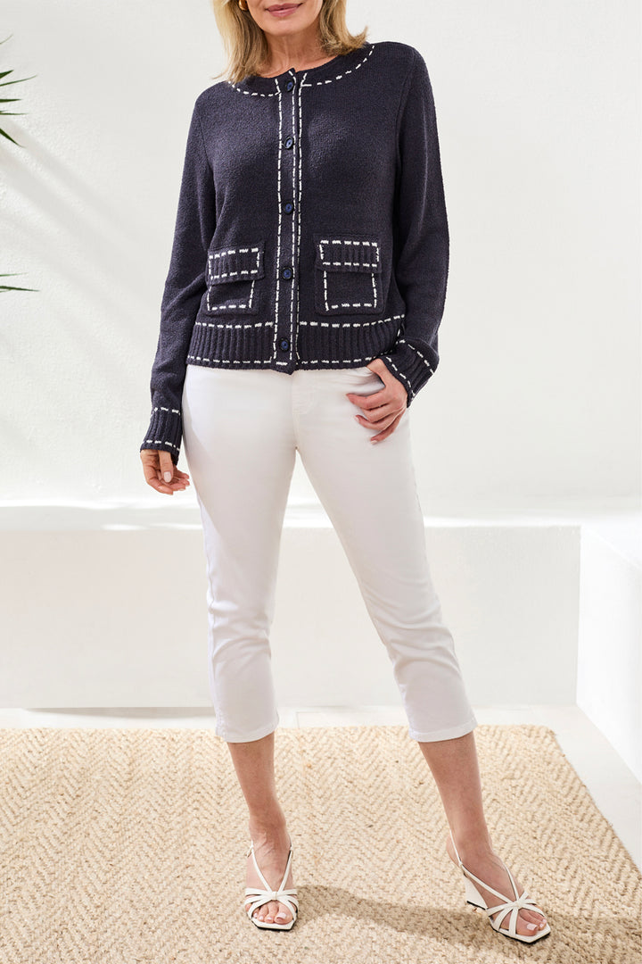 Woman wearing a navy blue sweater with white trim and white pants on a neutral background