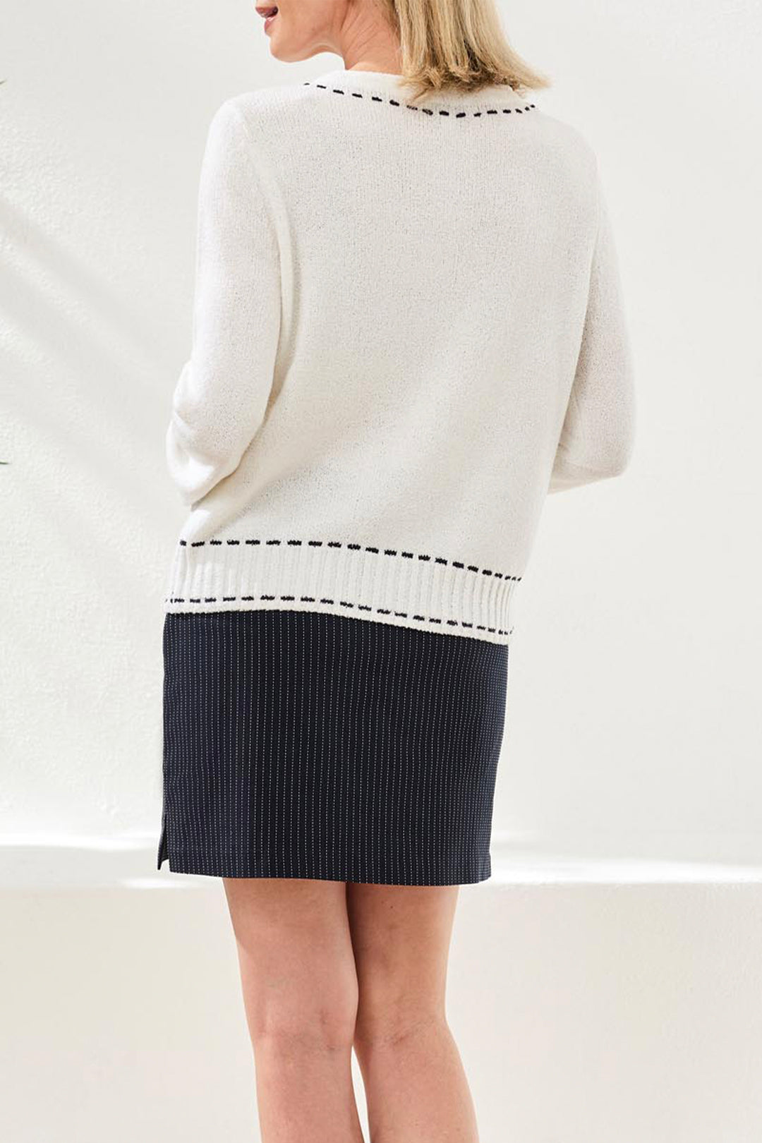 Person wearing a white sweater with black trim and a black skirt on a light background