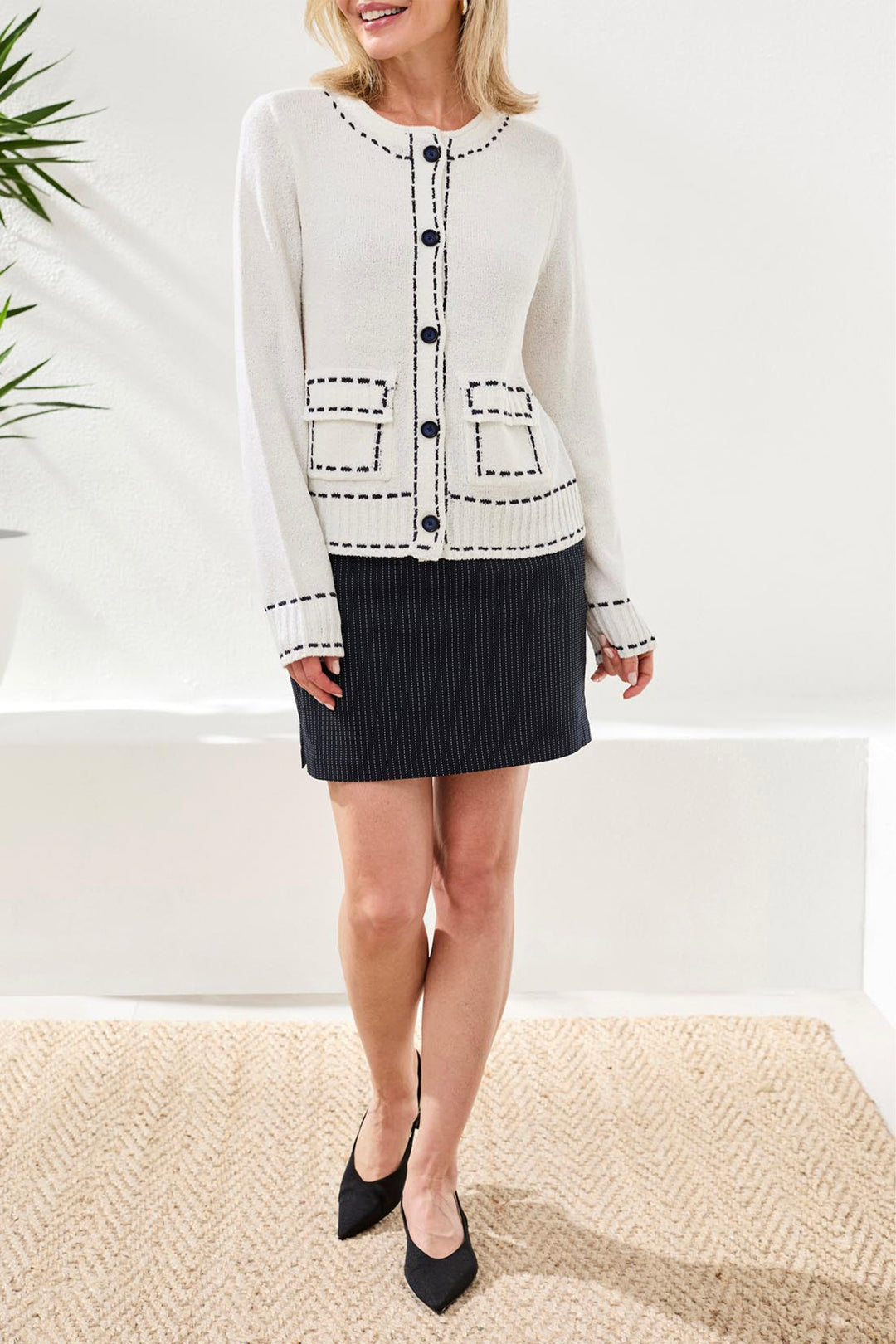 Woman wearing a white patterned cardigan over a black skirt with a white background