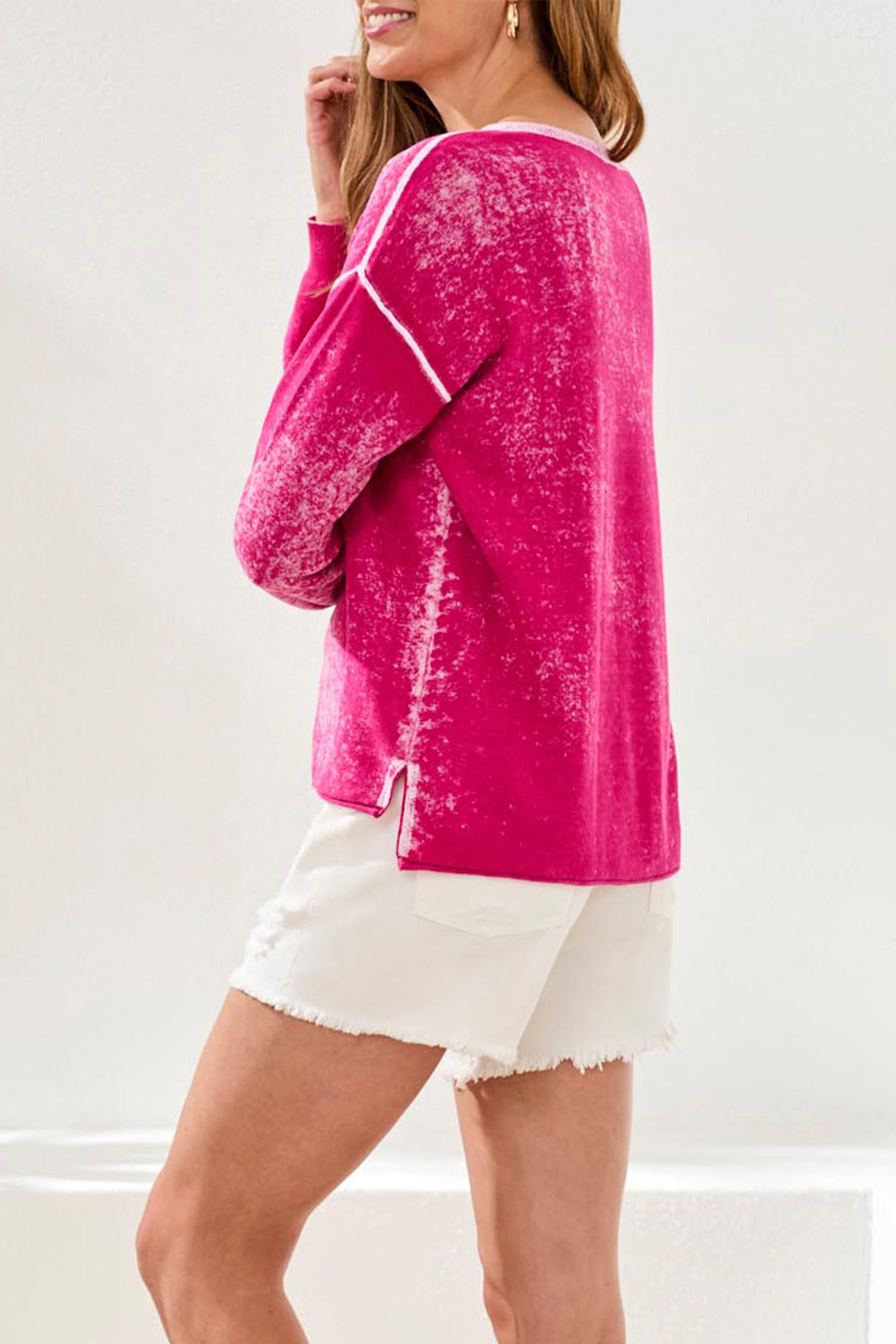 Woman wearing a pink distressed sweater and white shorts on a plain background