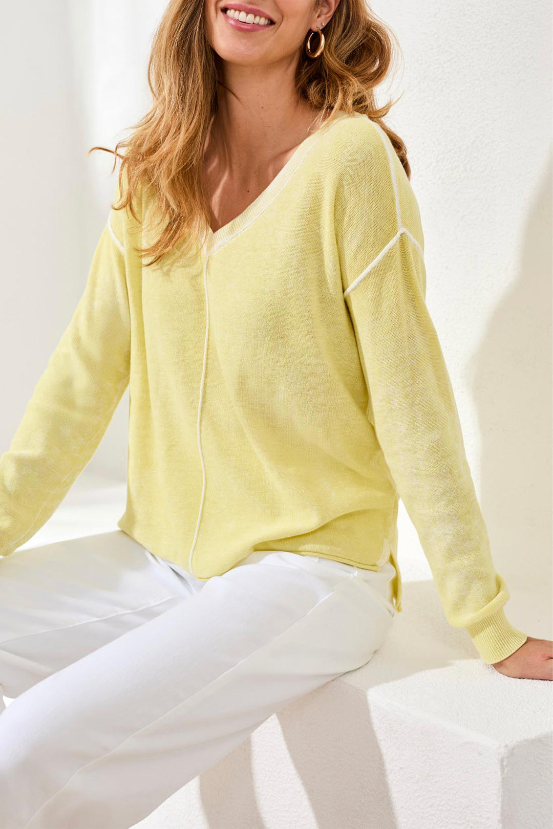 Woman wearing a light yellow sweater and white pants against a white background