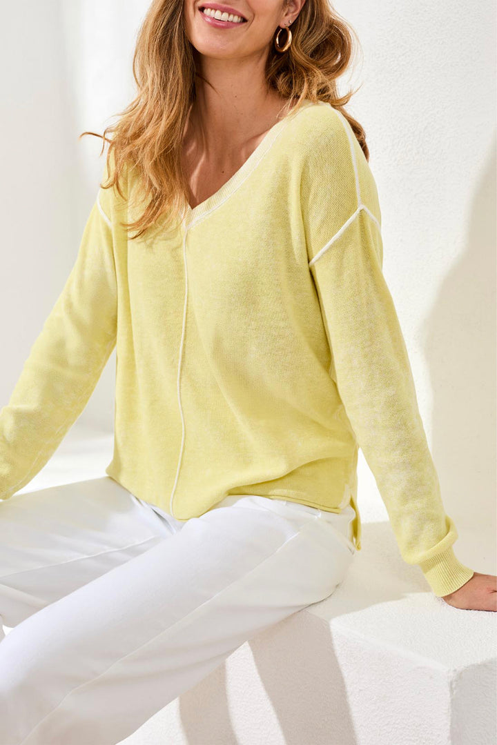 Woman wearing a light yellow sweater and white pants against a white background