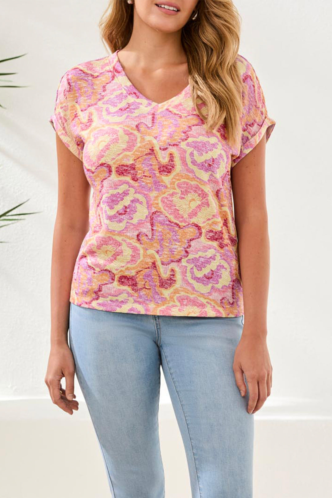 Woman wearing a pink and yellow patterned top with light blue jeans on a white background