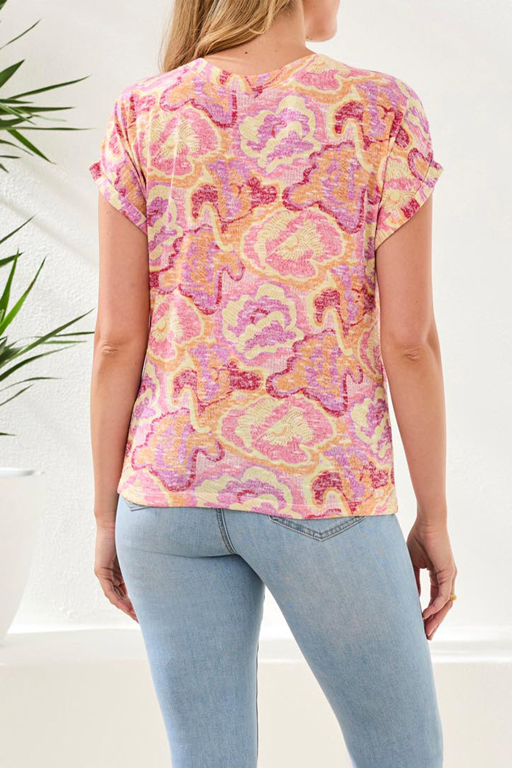 Person wearing a colorful patterned top and light blue jeans against a white background