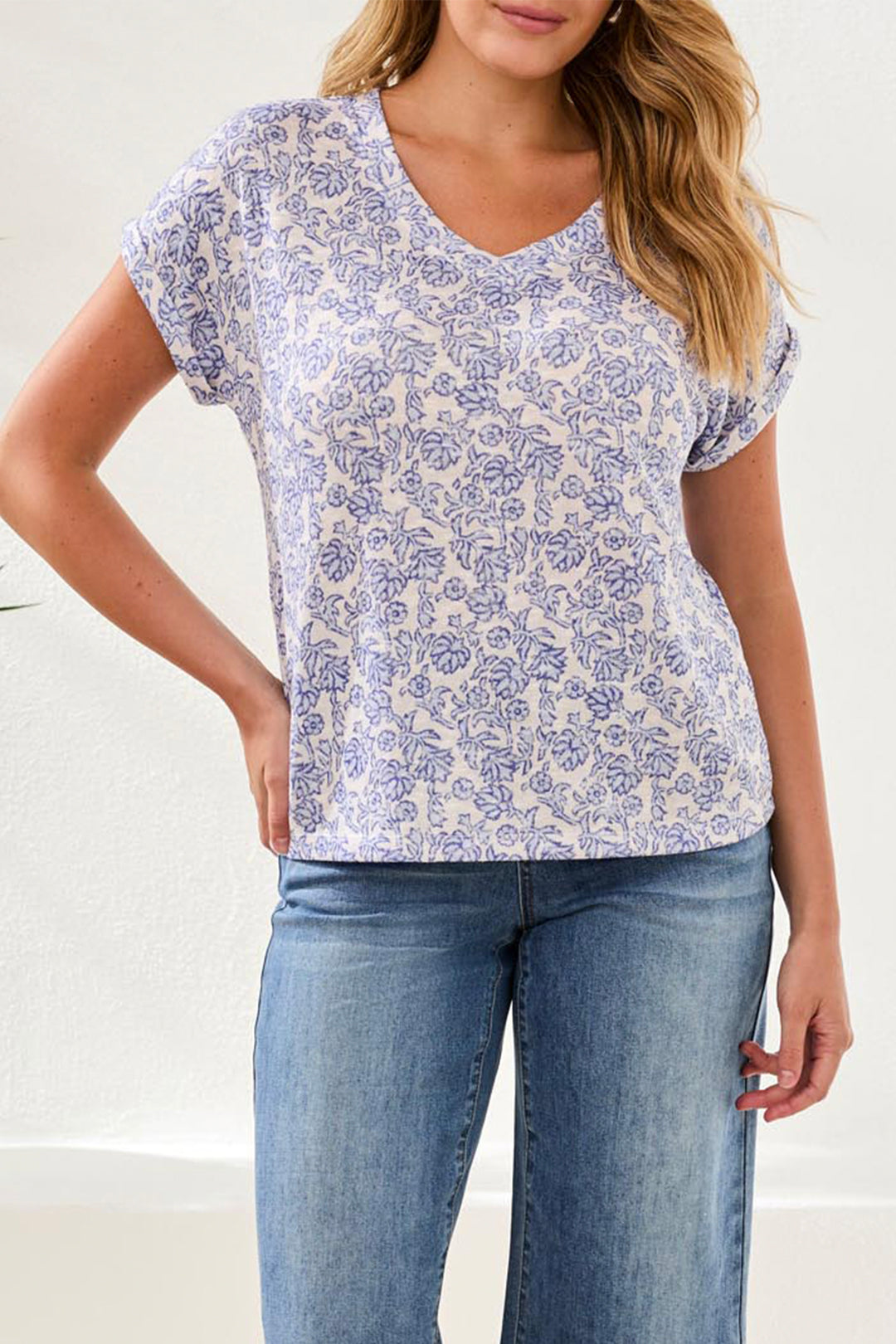 Woman wearing a blue and white floral patterned shirt with jeans on a plain background