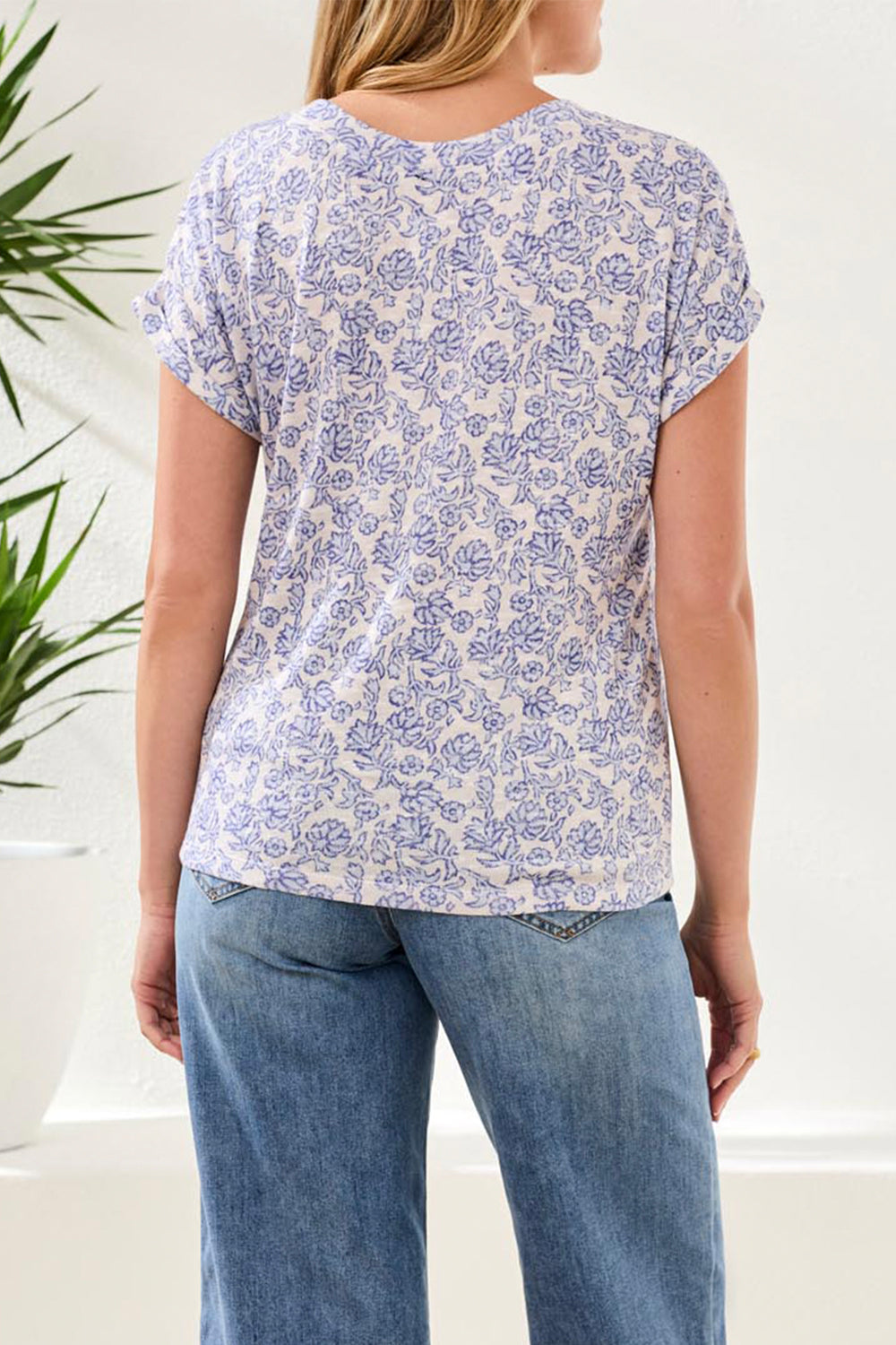 Woman wearing a blue floral patterned shirt and jeans indoors with a plant in the background
