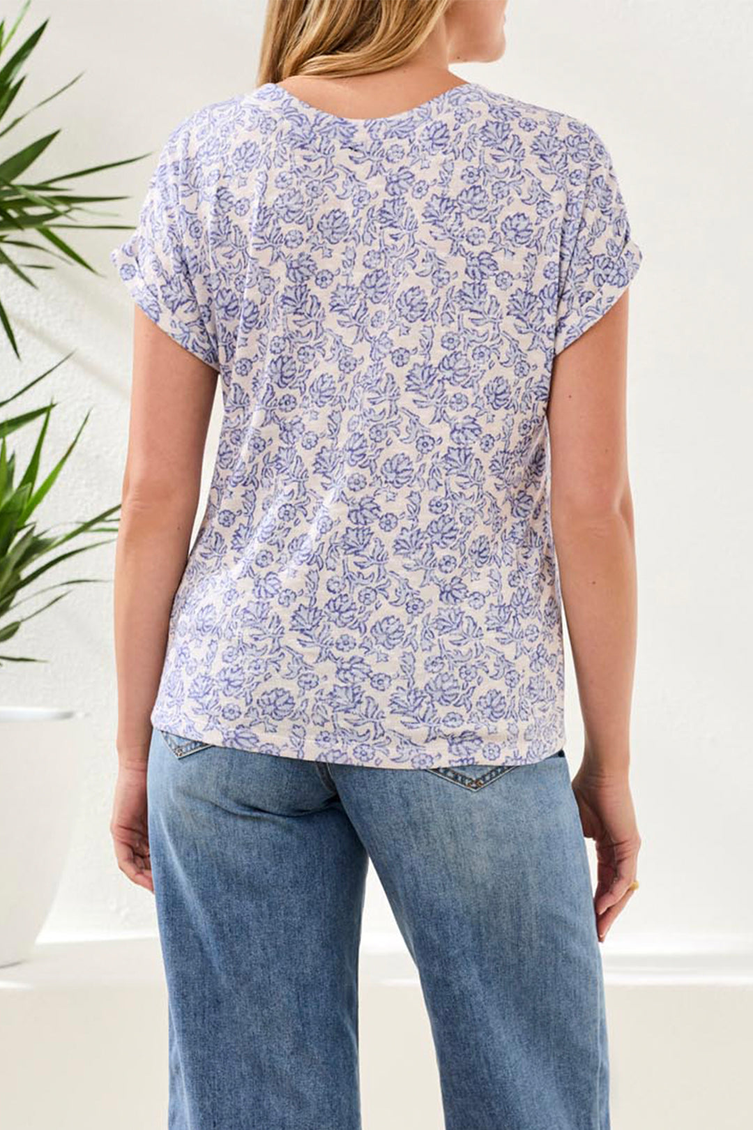 Woman wearing a blue floral patterned shirt and jeans indoors with a plant in the background