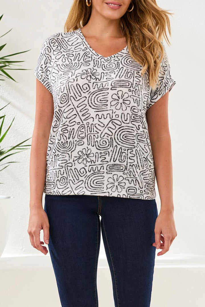 Woman wearing a black and white patterned top with blue jeans against a white background