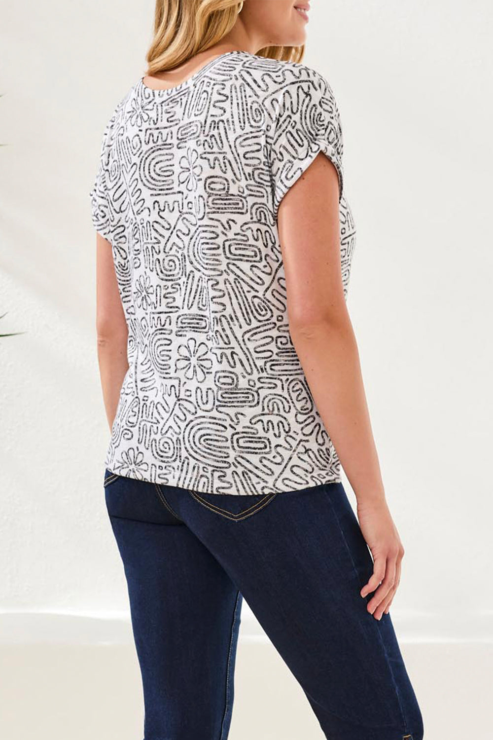 Woman wearing a white t-shirt with black abstract patterns and dark blue jeans on a white background