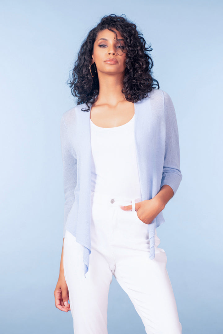 Woman wearing a light blue cover up cardigan over a white top and pants against a light blue background