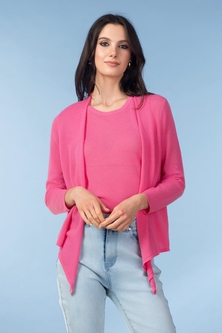 Woman wearing a pink cover up cardigan over a pink top and light blue jeans on a light blue background