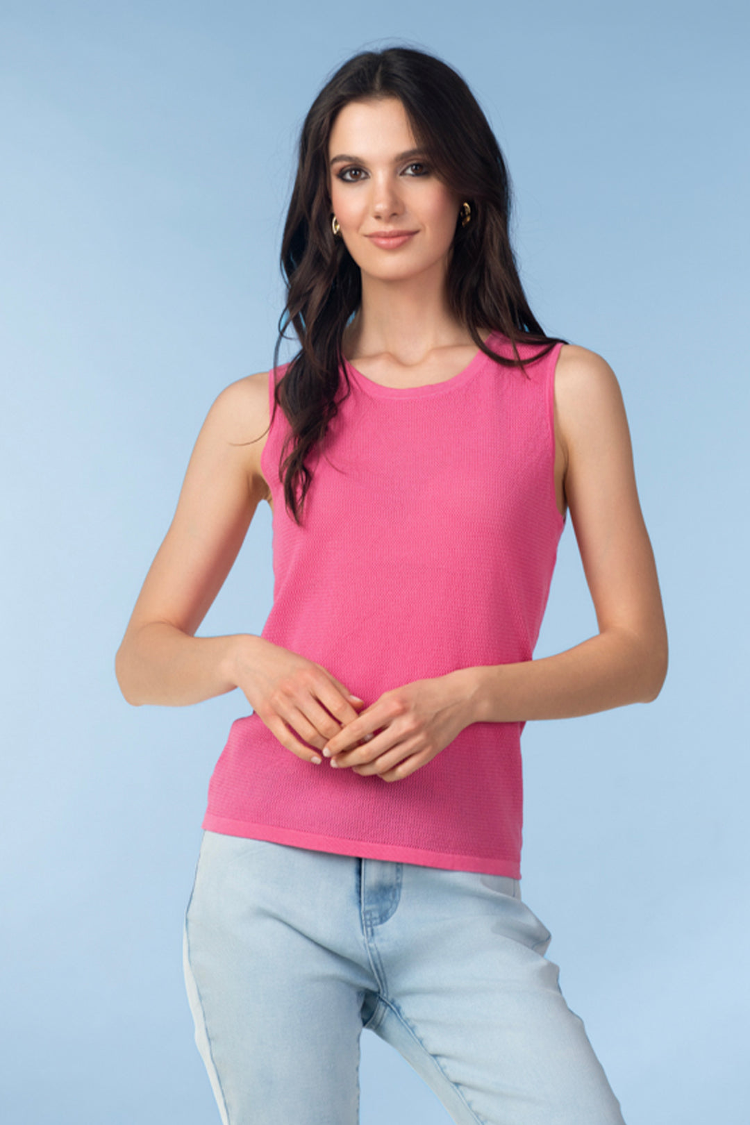 Woman wearing a pink sleeveless top and light blue jeans against a light blue background