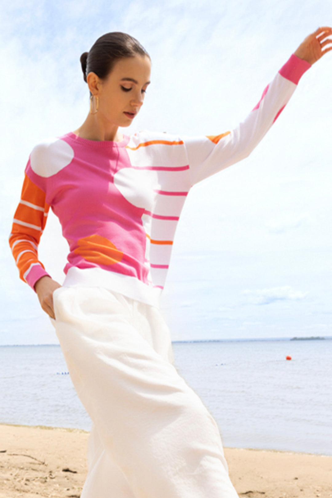 Woman wearing a colorful striped sweater and white pants on a beach.