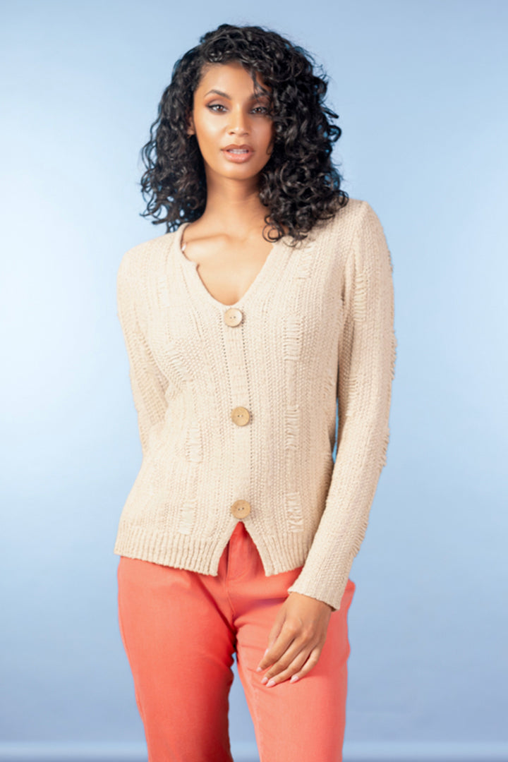 Woman wearing a beige cardigan and pink pants against a light blue background