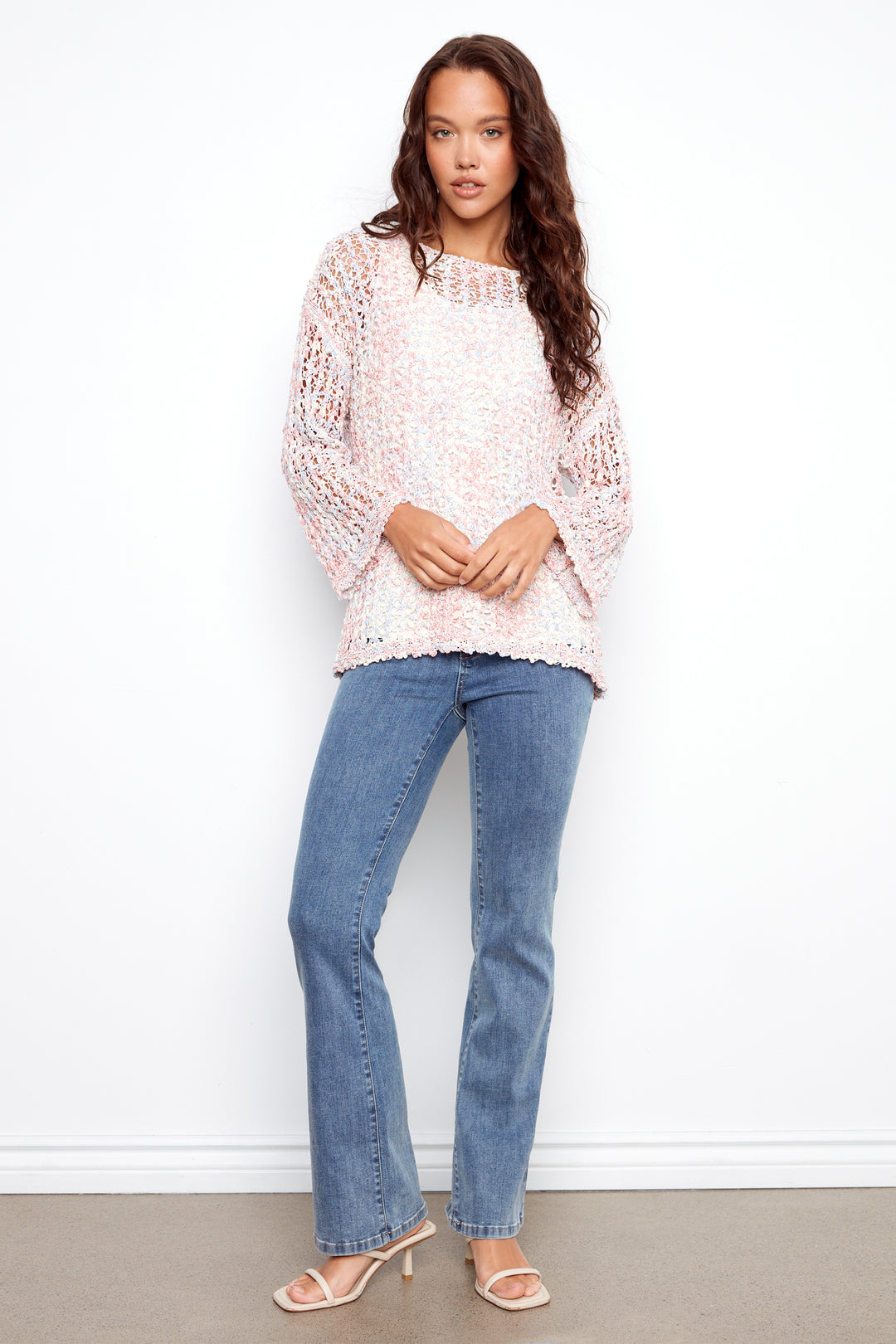 Woman wearing a light pink lace top and blue jeans against a white background