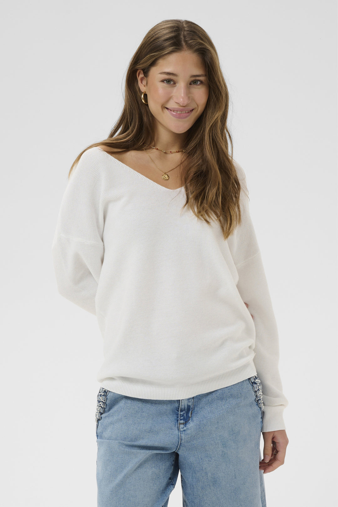 Woman wearing a white sweater and blue jeans on a plain background